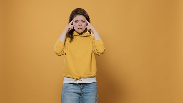 Donna concentrata che pensa e si concentra con un'idea toccando le tempie con il dito indice contemplando l'uso dell'immaginazione in studio. Giovane casual che indossa una felpa con cappuccio che ha pensieri stimolanti.