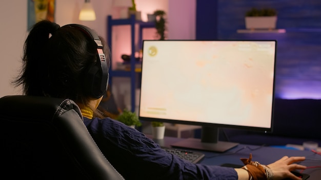 Donna concentrata del giocatore che perde il gioco multiplayer virtuale su un computer potente a casa con cuffie professionali