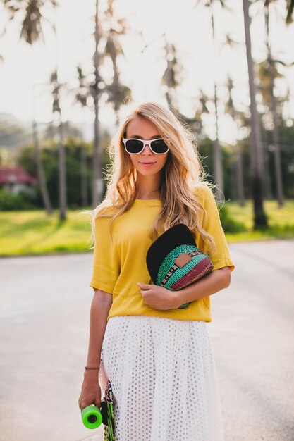 Donna cool hipster con skateboard e cappuccio in posa sorridente in vacanza