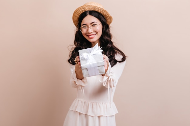 Donna coreana allegra che mostra regalo. Modello asiatico di risata in cappello che tiene casella attuale.