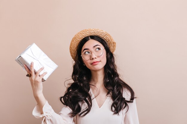 Donna coreana pensierosa che tiene casella attuale. Studio shot di sognante ragazza cinese con regalo.