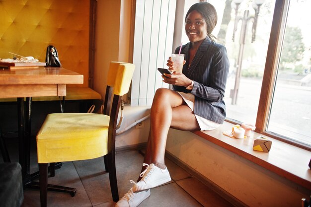 Donna d'affari afroamericana che beve limonata cocktail nella caffetteria Ragazza nera che riposa con il telefono cellulare