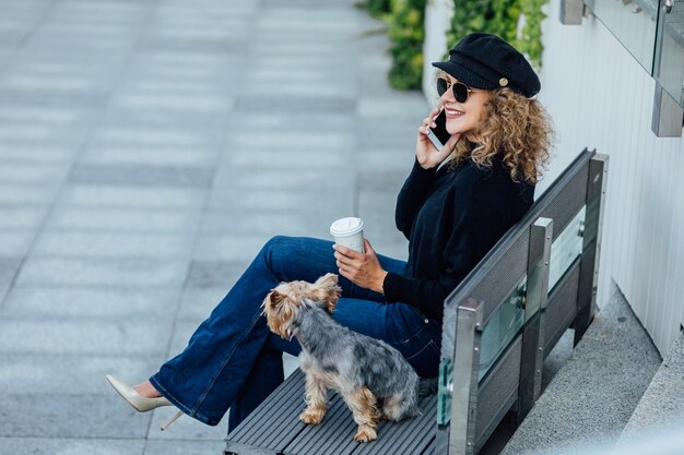 Donna d'affari che cammina lungo la strada europea con un piccolo cane di razza Chihuahua di due colori al guinzaglio nuvoloso caldo autunno primavera tempo ragazza vestita con camicia nera e scarpe nude