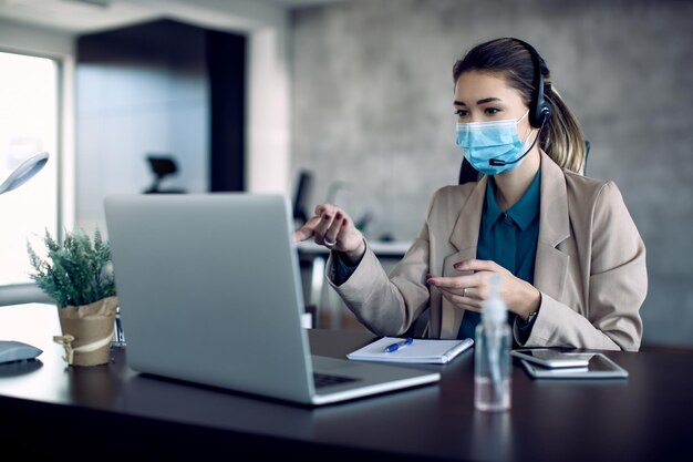 Donna d'affari che ha una chiamata in conferenza su laptop dall'ufficio a causa della pandemia COVID19