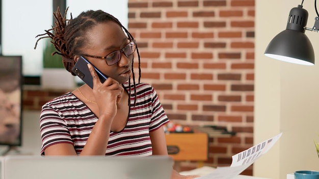 Donna d'affari che parla con le persone su una chiamata smartphone, utilizzando la linea telefonica delle telecomunicazioni per chattare con il manager e lavorare in remoto da casa. Chatta al telefono, lavoro d'ufficio freelance.