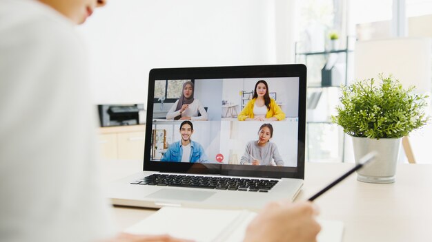 donna d'affari che utilizza il laptop parla con i colleghi del piano in una riunione di videochiamata mentre si lavora da casa in soggiorno.