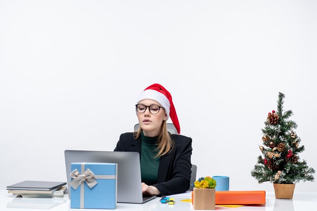 Donna d'affari con un cappello di Babbo Natale seduto a un tavolo con un albero di Natale e un regalo