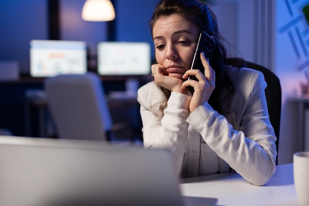 Donna d'affari concentrata durante la telefonata che lavora dall'ufficio commerciale discutendo con un collega per i grafici finanziari