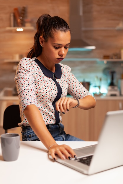 Donna d'affari esaurita che controlla il tempo di guardia prima della scadenza del progetto. Dipendente che utilizza la tecnologia moderna a mezzanotte facendo gli straordinari per lavoro, affari, impegni, carriera, rete, stile di vita, wireless.