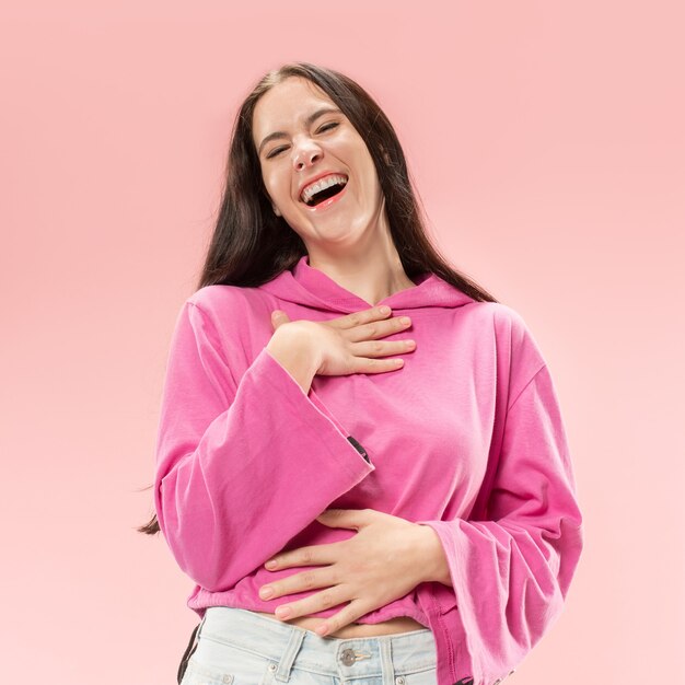 Donna d'affari felice in piedi e sorridente isolato su sfondo rosa studio. Bellissimo ritratto femminile a mezzo busto. Giovane donna emotiva. Le emozioni umane, il concetto di espressione facciale