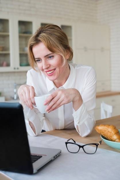 Donna d&#39;affari gioiosa con caffè usando il portatile