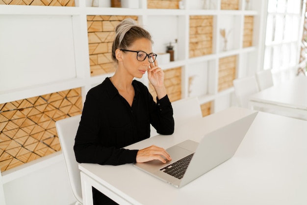 Donna d'affari in abito casual elegante seduto in ufficio e utilizzando il laptop