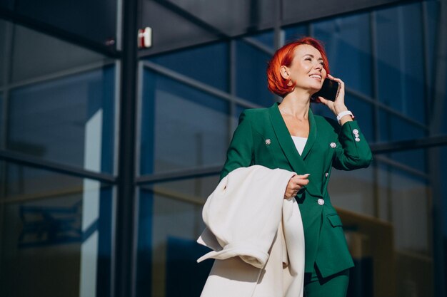 Donna d'affari in abito verde che usa il telefono fuori dalla strada