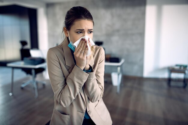Donna d'affari malata che soffia il naso mentre si lavora in ufficio