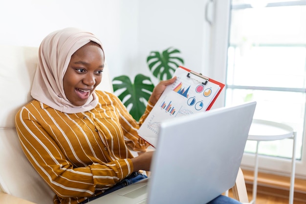 Donna d'affari musulmana focalizzata che presenta grafici e grafici durante la videochiamata online Giovane donna d'affari ih hijab che ha una chiamata in conferenza con il cliente sul computer portatile che lavora al chiuso