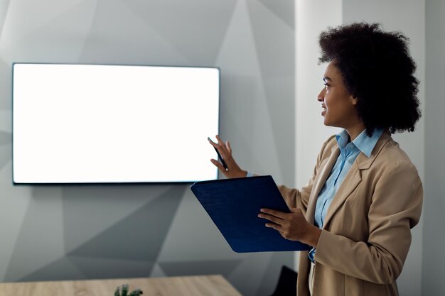 Donna d'affari nera che parla con qualcuno durante la videoconferenza sullo schermo di proiezione in ufficio