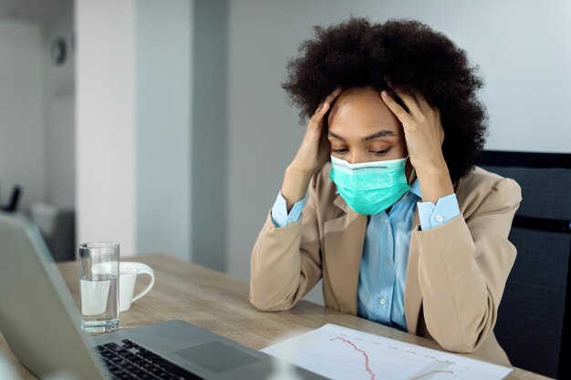 Donna d'affari nera che si sente stressata mentre lavora in ufficio durante la pandemia di coronavirus
