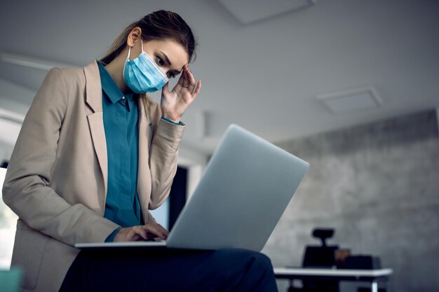 Donna d'affari sconvolta che lavora su un computer in ufficio durante la pandemia di coronavirus