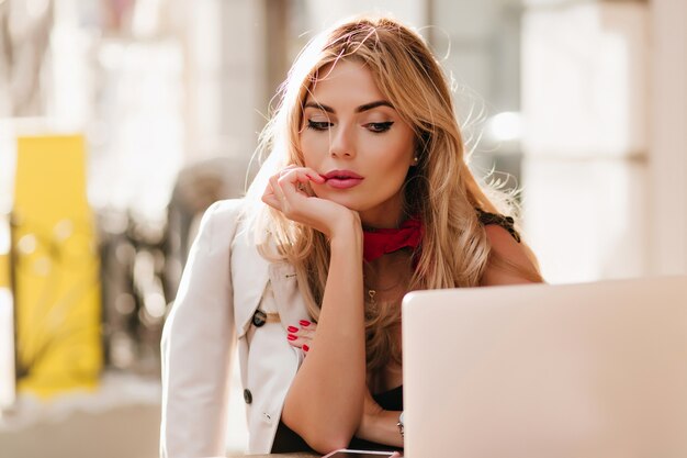 Donna d'affari stanca con trucco scintillante guardando lo schermo del laptop mentre era seduto al caffè