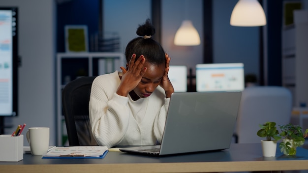 Donna d'affari stressata che soffre di mal di testa al lavoro facendo gli straordinari a tarda notte