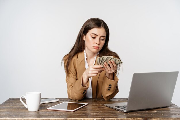 Donna d'affari triste che conta i soldi in ufficio con la faccia delusa sconvolta a basso reddito che posa contro chi...