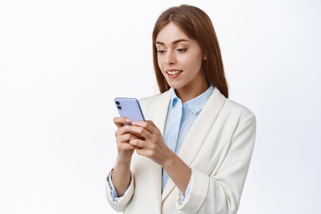 Donna d'ufficio professionale ceo che legge lo schermo del telefono cellulare in piedi in giacca e cravatta e utilizza l'app per smartphone in piedi con il cellulare su sfondo bianco
