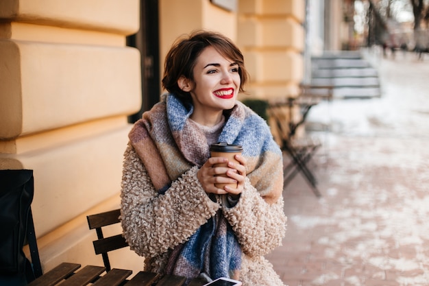 Donna dai capelli corti entusiasta che beve caffè in città