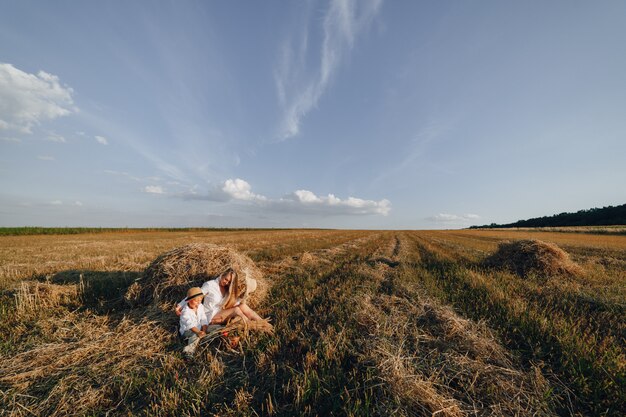 Donna dai capelli lunghi abbastanza bionda con figlio piccolo biondo al tramonto rilassante nel campo e assaporando la frutta da un cestino di paglia. estate, agricoltura, natura e aria fresca in campagna.