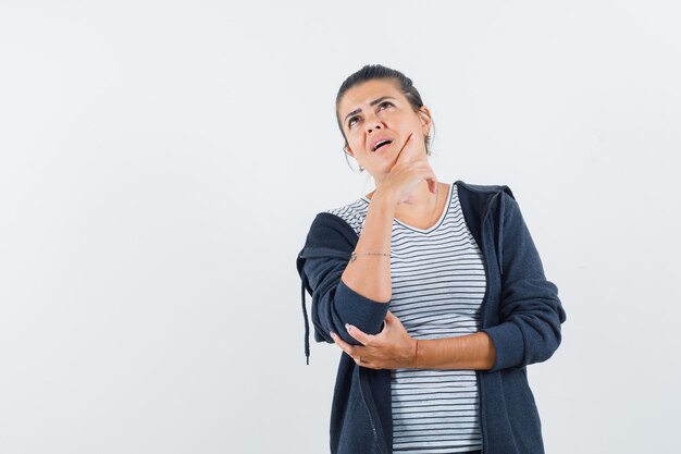 Donna dai capelli scuri in posa come pensare qualcosa in camicia