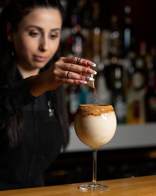 Donna del barista che aggiunge la polvere di cannella nel cocktail latteo.