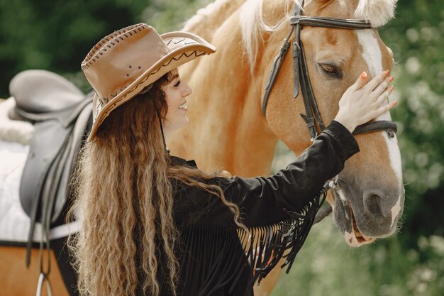 Donna del cavaliere che parla con il suo cavallo in un ranch. La donna ha i capelli lunghi e vestiti neri. Equestre femminile che tocca un cavallo.