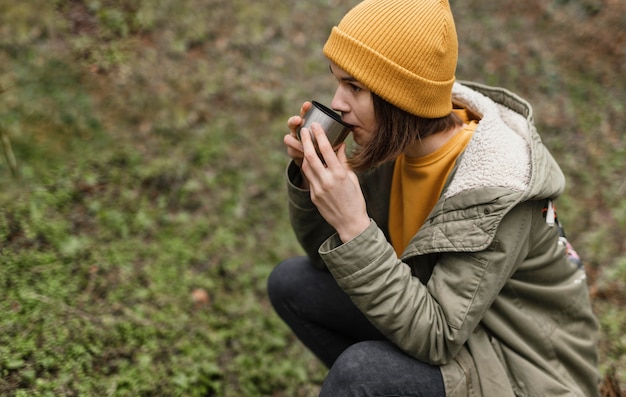 Donna del colpo medio che beve caffè nella foresta