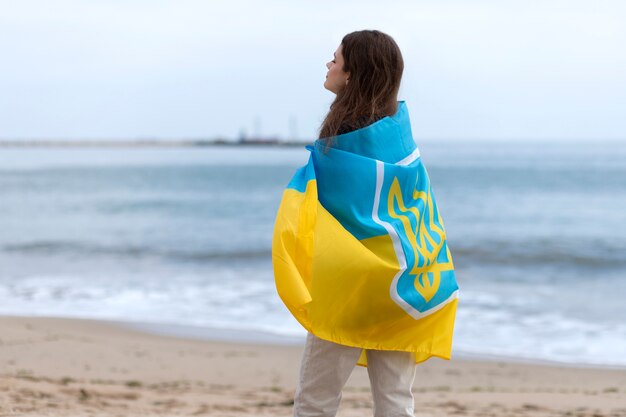 Donna del colpo medio che indossa la bandiera ucraina in spiaggia