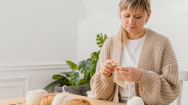 Donna del colpo medio che lavora a maglia a casa