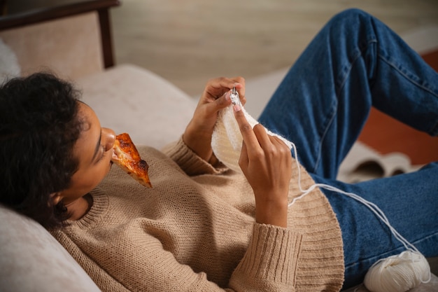 Donna del colpo medio che lavora a maglia sul pavimento