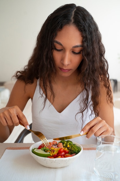 Donna del colpo medio che mangia ciotola di salmone