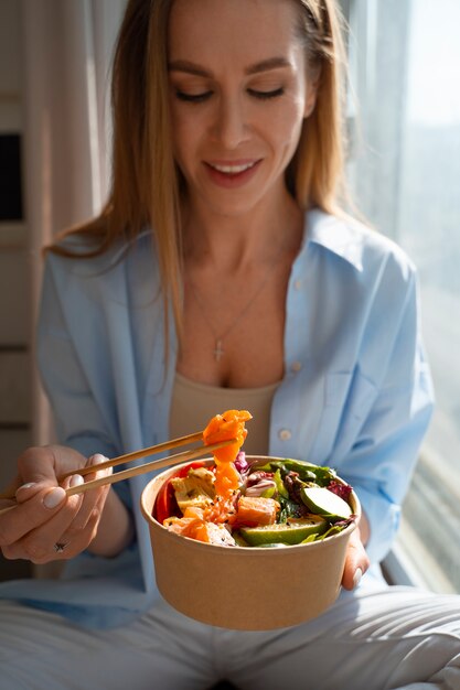 Donna del colpo medio che mangia ciotola di salmone