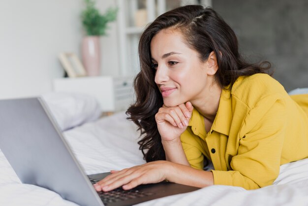 Donna del colpo medio che si siede nel letto con il computer portatile