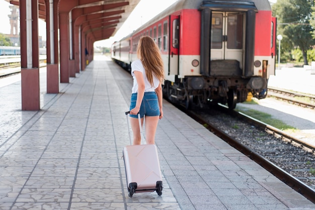 Donna del colpo pieno che cammina con i bagagli nella stazione ferroviaria