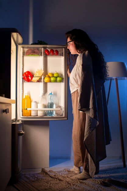 Donna del colpo pieno che controlla il frigorifero