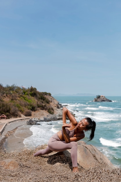 Donna del colpo pieno che fa yoga al mare