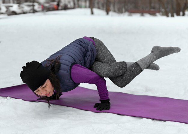 Donna del colpo pieno che fa yoga nella stagione fredda