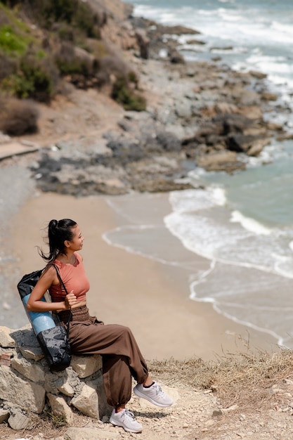 Donna del colpo pieno con la stuoia di yoga alla spiaggia