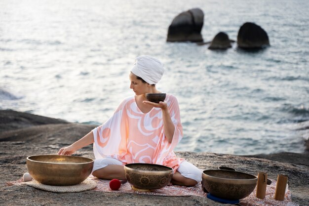 Donna del colpo pieno con le campane tibetane sulla spiaggia