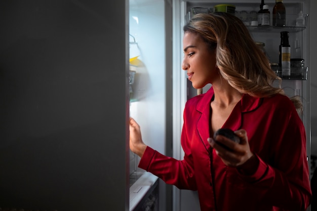 Donna del piano medio che controlla il frigorifero di notte