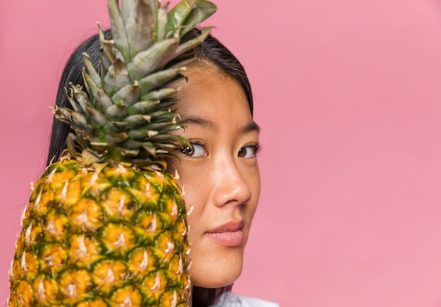 Donna del primo piano che tiene un ananas e che esamina macchina fotografica