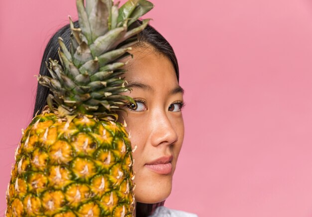 Donna del primo piano che tiene un ananas e che esamina macchina fotografica