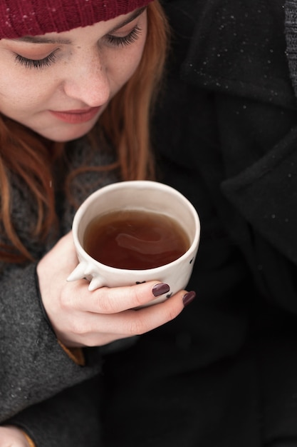 Donna del primo piano con i vestiti di inverno che tengono tazza di tè