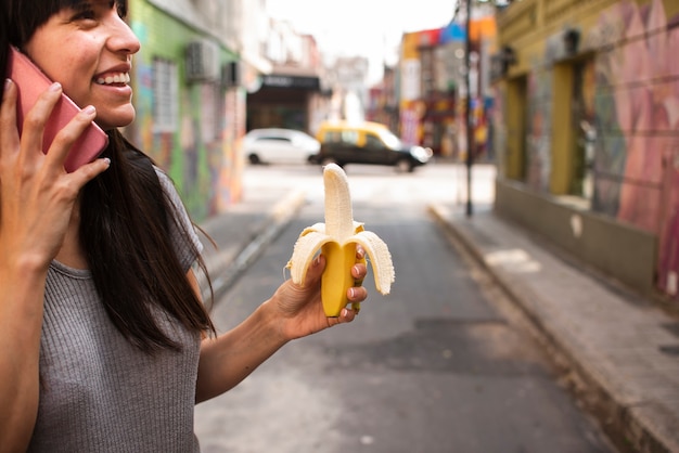 Donna del primo piano con la banana che intraprende il telefono