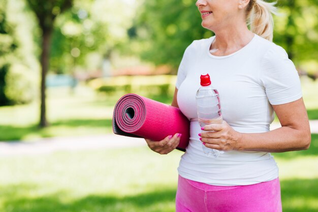 Donna del primo piano con la stuoia di yoga all'aperto